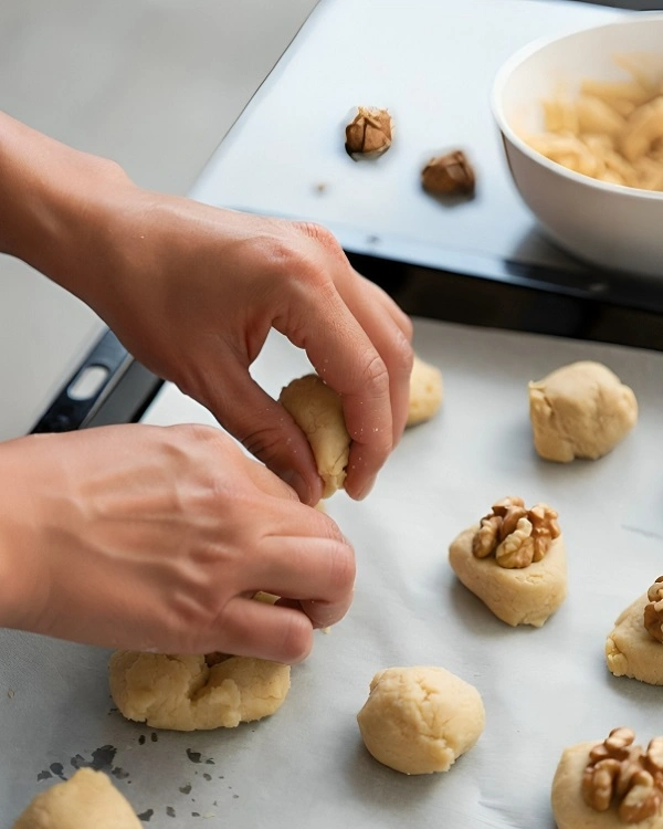 Homemade Albanian sheqerpare dough being shaped by hand on a baking tray with walnuts placed on top