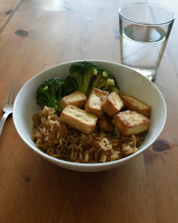 Homemade crispy tofu with brown rice and steamed broccoli served in a bowl.