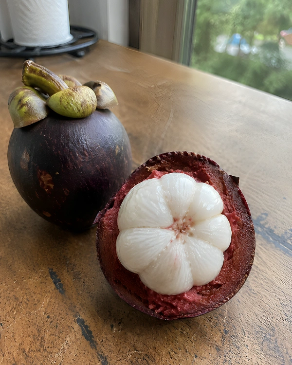 A whole purple mangosteen next to a halved one revealing its soft white juicy segments on a wooden surface.