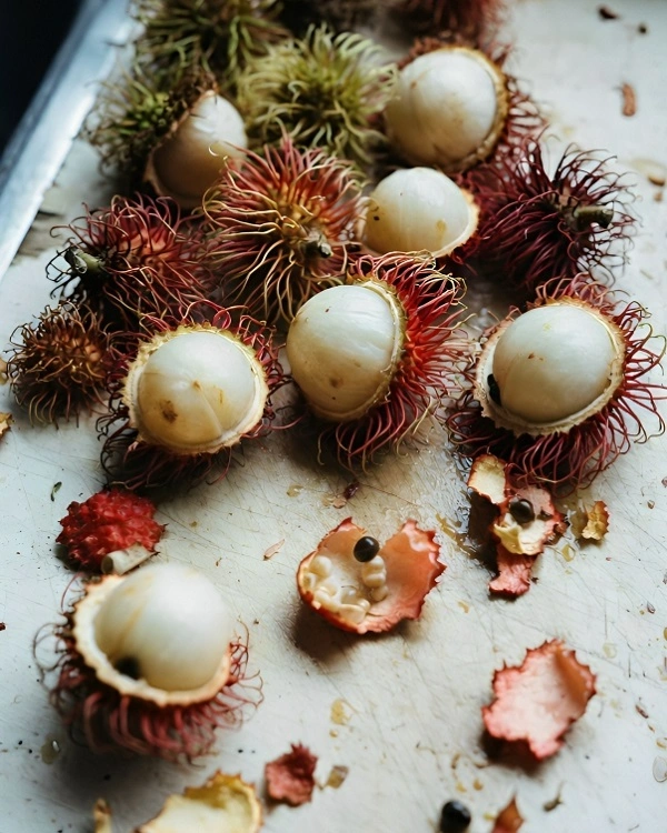 A pile of red hairy rambutan fruits peeled open to show the translucent white flesh and seeds on a cutting board.
