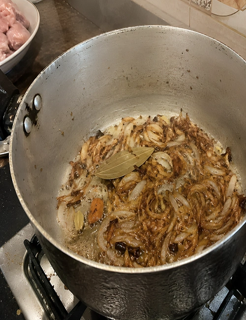 Sliced onions and whole fragrant spices frying in a cooking pot until golden brown