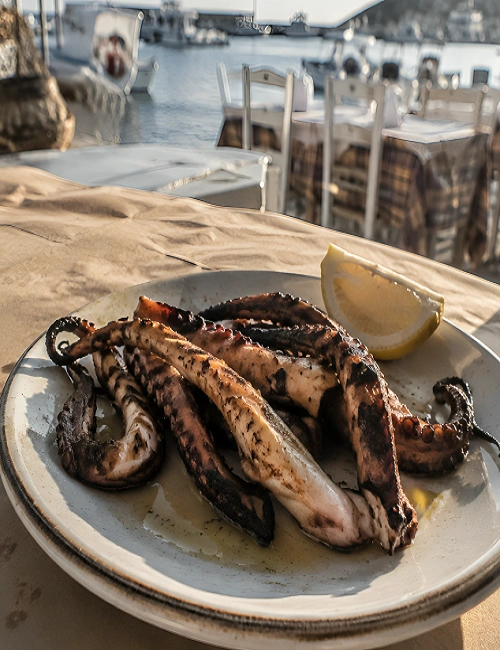Charred octopus tentacles on a plate served with a fresh lemon wedge.