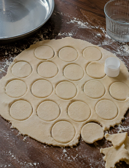 Thinly rolled dough cut into small round puri shapes using a bottle cap.