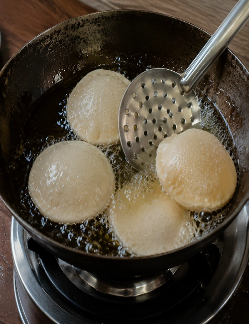 Puris puffing up while deep frying in hot oil in a pan.