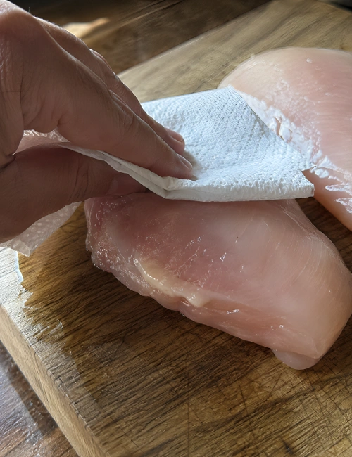 Drying a raw chicken breast with a paper towel