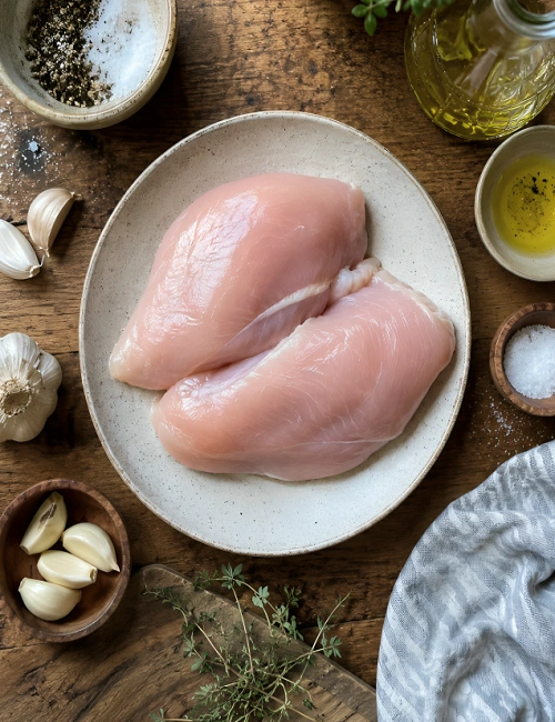 Raw chicken breasts on a plate with garlic and spices