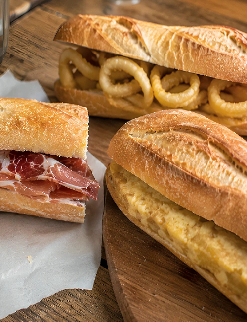 Three different types of Spanish bocadillos including fried calamari, potato omelette, and jamon serrano.