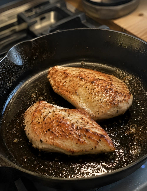 Two chicken breasts cooking in a black skillet