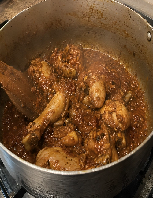 Bone-in chicken pieces coated and searing in a rich tomato onion masala paste