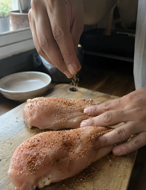 Sprinkling spices over raw chicken breasts