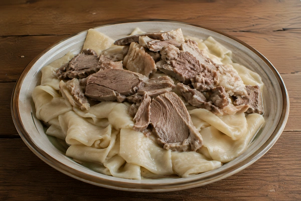 Tender slices of boiled beef layered over broad, flat handmade noodles in a shallow ceramic bowl.