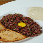 French beef tartare recipe with egg yolk served with toasted bread on white plate