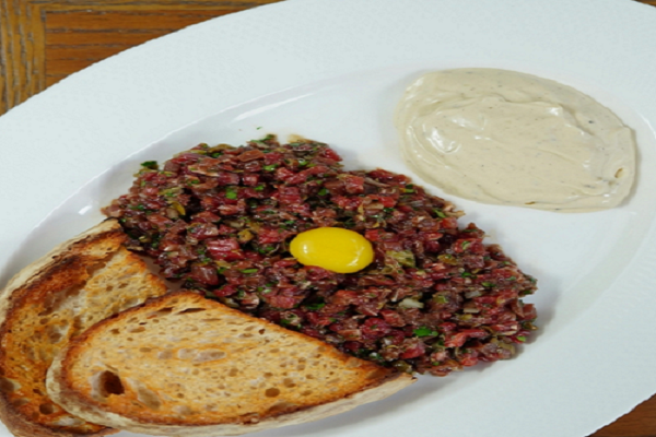 French beef tartare recipe with egg yolk served with toasted bread on white plate