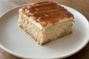A slice of Trileçe three milk cake topped with caramel glaze on a ceramic plate