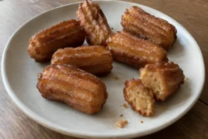 Golden-brown Tulumba fried dough pieces on a ceramic plate