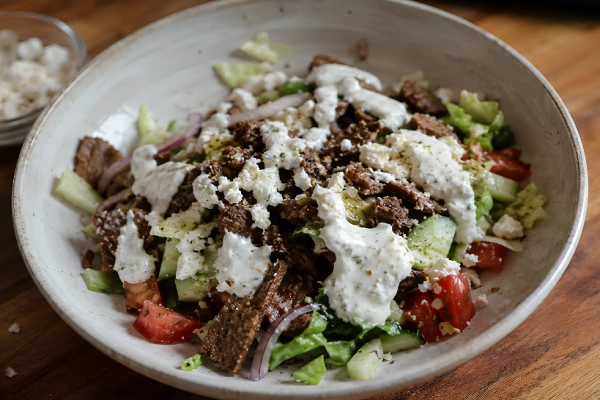 Homemade gyro salad with tzatziki dressing, feta cheese, fresh vegetables, and seasoned meat in a ceramic bowl