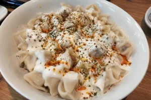 Authentic Turkish manti dumplings topped with garlic yogurt, melted butter, red pepper flakes, and dried mint served in a white bowl on a wooden table