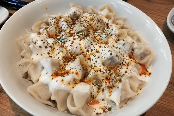 Authentic Turkish manti dumplings topped with garlic yogurt, melted butter, red pepper flakes, and dried mint served in a white bowl on a wooden table