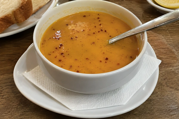Mercimek çorbası (Turkish red lentil soup) served in a white bowl with bread and chili flakes on a wooden table