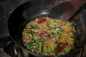 Whole spices blooming in hot oil with curry leaves, cumin seeds, and dried chilies in a pan