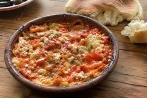 Traditional Albanian Fërgesë with peppers, tomatoes, and gjizë cheese served in a rustic clay dish with bread