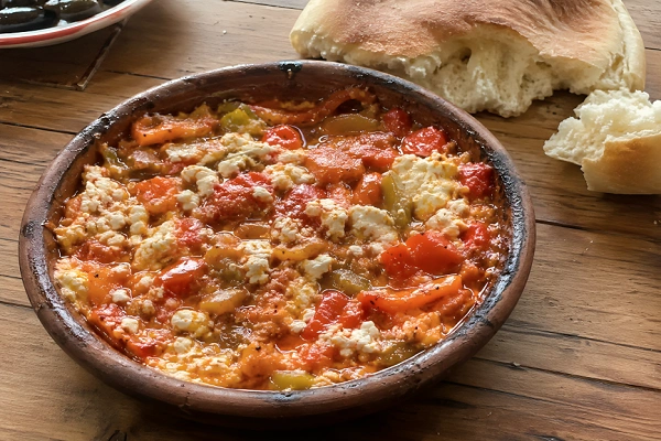 Traditional Albanian Fërgesë with peppers, tomatoes, and gjizë cheese served in a rustic clay dish with bread