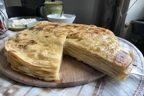 Traditional Albanian Flija recipe showing layered pastry cooked with butter and cream, sliced on a wooden serving board