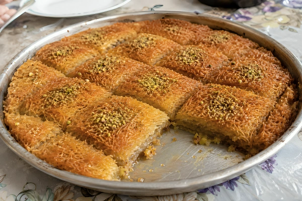 Golden-brown kadaif pastry topped with crushed pistachios and cut into squares on a traditional baking tray