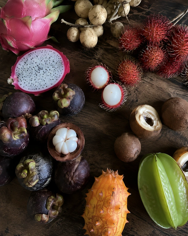 A colorful assortment of fresh exotic tropical fruits including dragon fruit, mangosteen, rambutan, and star fruit on a dark wooden table.