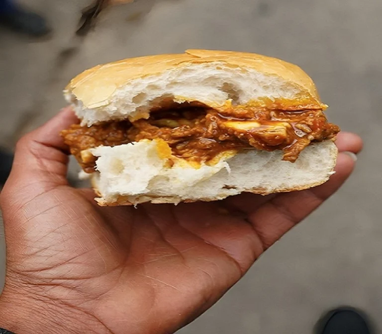 Street-style chicken burger held in hand with sauce dripping in a casual outdoor setting