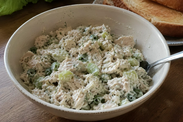 Creamy chicken salad with diced celery and green onions served in a ceramic bowl alongside toasted bread.