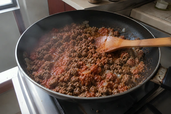 Ground beef and tomato sauce stirring together with a wooden spoon in a pan