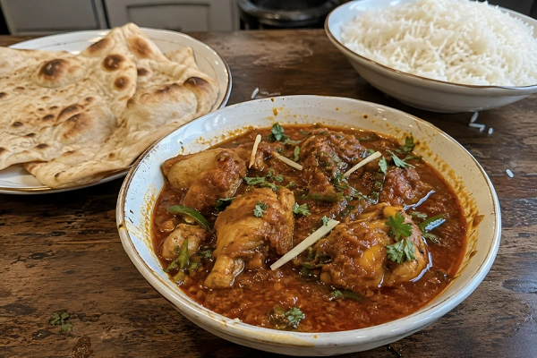 Freshly cooked chicken curry served in a white bowl alongside warm naan bread and steamed rice