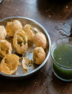 Crispy homemade pani puris stuffed with potato filling served next to a bowl of green mint water.
