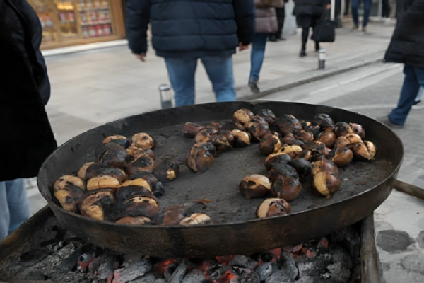 Fresh chestnuts roasting over a hot charcoal fire in a traditional metal pan on the street.