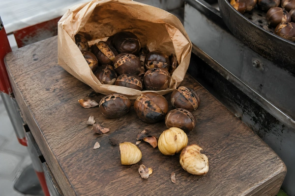 Warm roasted chestnuts spilling out of a brown paper bag with peeled soft chestnut flesh ready to eat.