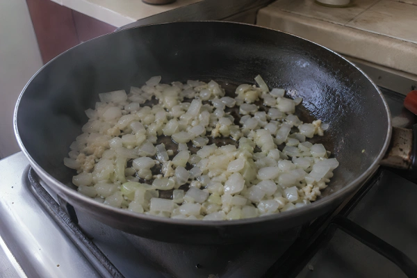 Chopped onions and minced garlic cooking in olive oil inside a black skillet