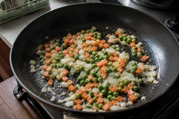 Diced carrots and green peas sautéing in a skillet.