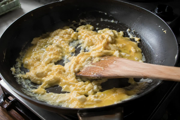 Scrambling beaten eggs in a pan with a wooden spatula