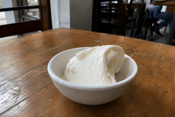 A single thick slice of white Maraş dondurma sitting inside a small white ceramic bowl on a wooden table.