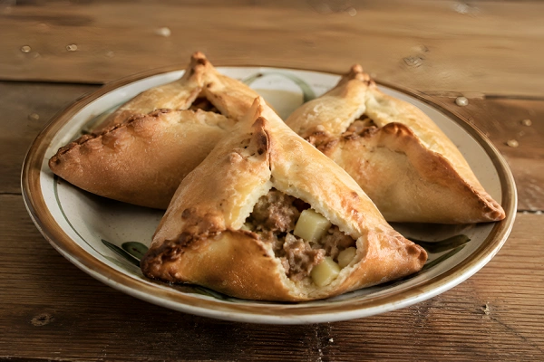 Three golden-baked triangular Echpochmak pastries filled with minced beef and diced potatoes served on a ceramic plate.