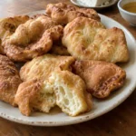 Freshly fried golden Albanian petulla served on a ceramic plate with feta cheese, honey, and jam on the side.