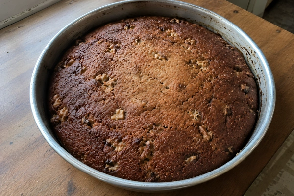 Freshly baked dark golden Shendetlie cake cooling in a round baking pan.