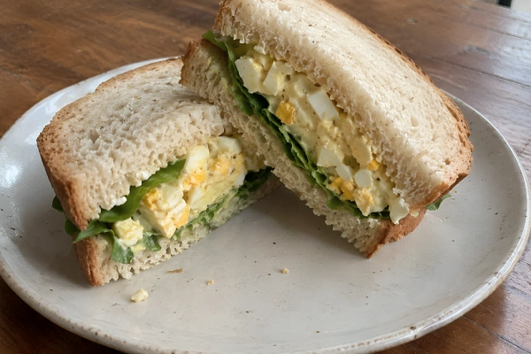 Egg salad sandwich layered with green lettuce on sliced whole wheat bread.