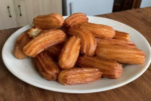 A white plate filled with golden crispy syrup soaked Turkish tulumba pastries