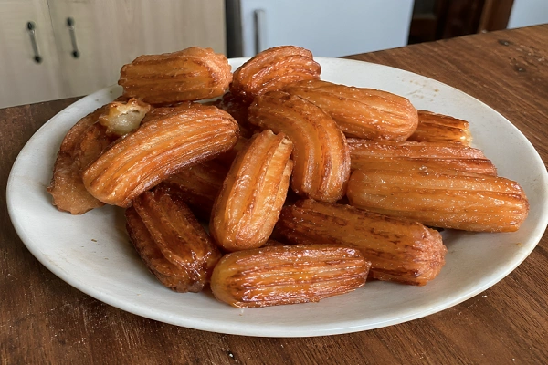 A white plate filled with golden crispy syrup soaked Turkish tulumba pastries