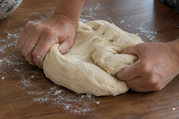 Hands working and folding yeast dough on a flour-dusted wooden tabletop