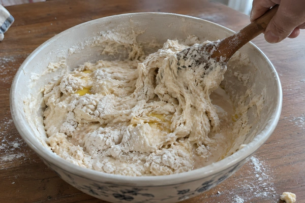 Wooden spoon bringing together flour yogurt and liquid in a ceramic mixing bowl