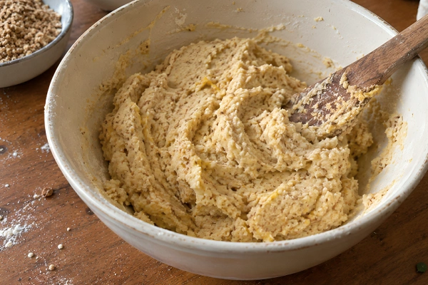 Soft cookie dough mixed with ground walnuts in a cream ceramic bowl with a wooden spoon.
