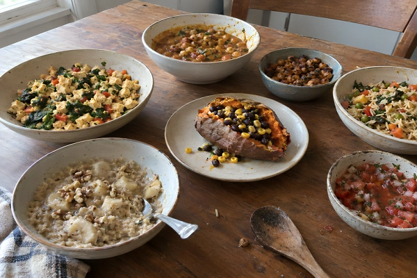 A rustic wooden dining table spread with various oil-free vegan dishes served in ceramic bowls.
